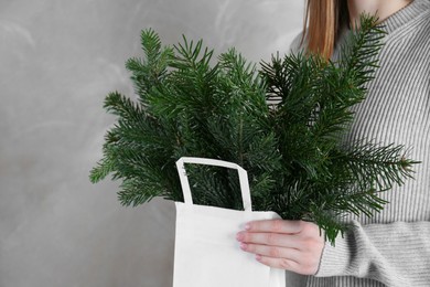 Photo of Woman holding green fir branches in paper bag near gray wall, closeup. Christmas decor