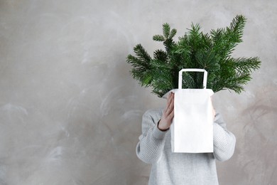 Photo of Woman holding green fir branches in paper bag near gray wall, space for text. Christmas decor