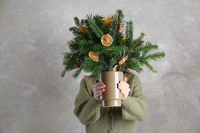 Photo of Woman holding beautiful Christmas composition of fir tree branches decorated with dried orange slices and cinnamon sticks near gray wall