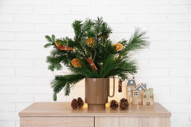 Photo of Beautiful Christmas composition of decorated fir and pine tree branches on wooden nightstand near white brick wall