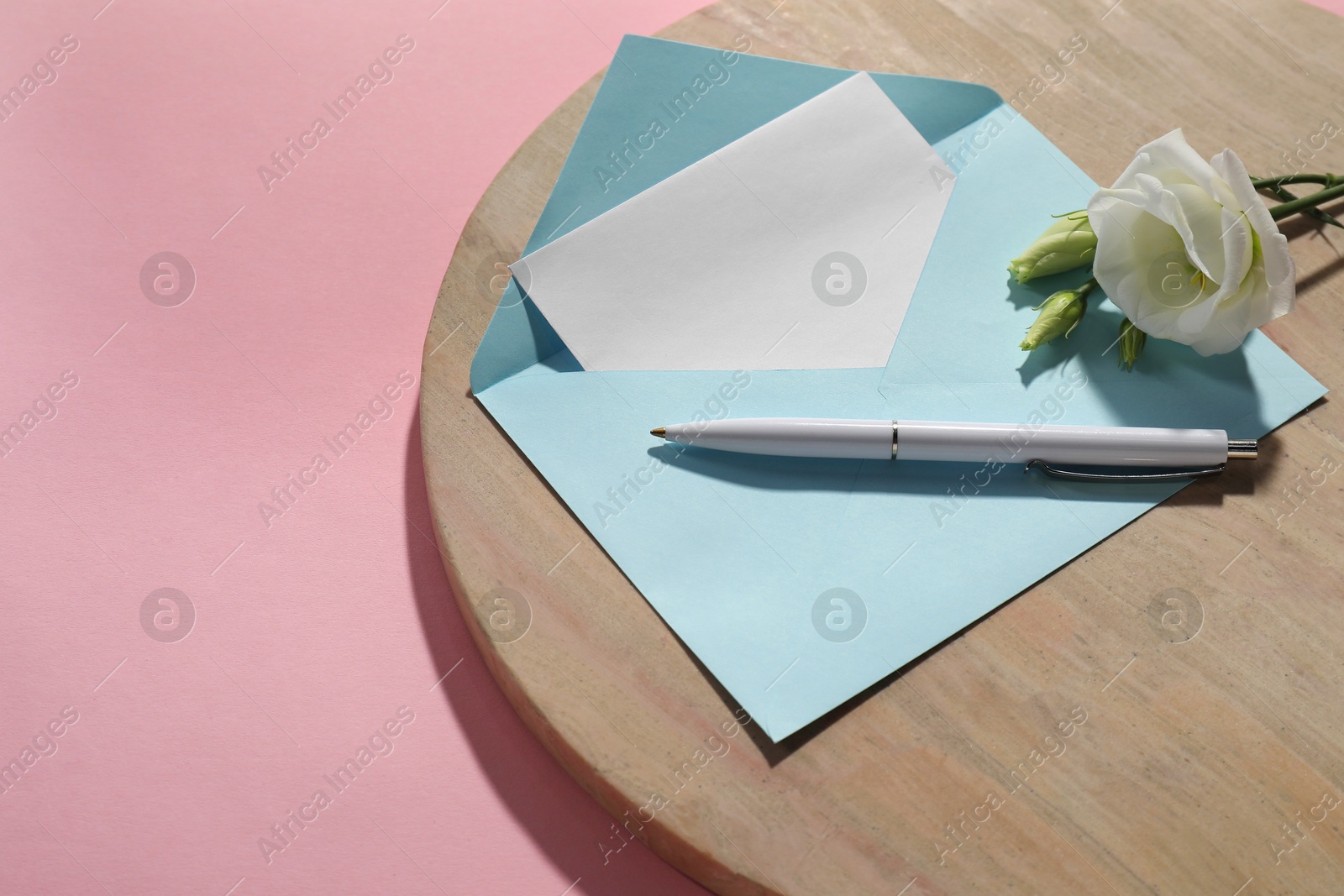 Photo of Paper envelope with letter, flower and pen on pink background, above view. Mockup for design