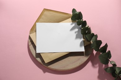 Photo of Kraft paper envelope with letter and eucalyptus branch on pink background, above view. Mockup for design