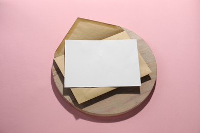 Photo of Kraft paper envelope with letter on pink background, above view. Mockup for design