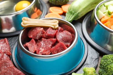 Photo of Pet food. Fresh beef in feeding bowl and chew bone among products on table, closeup