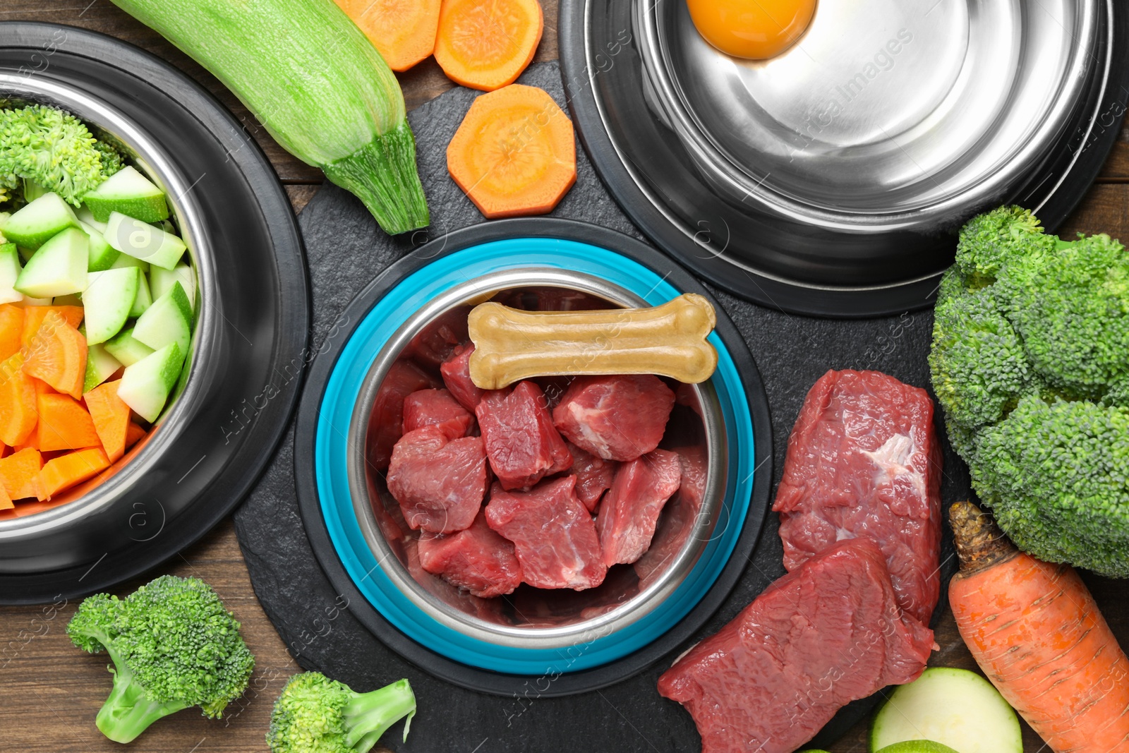 Photo of Pet food. Fresh beef in feeding bowl and chew bone among products on wooden table, flat lay