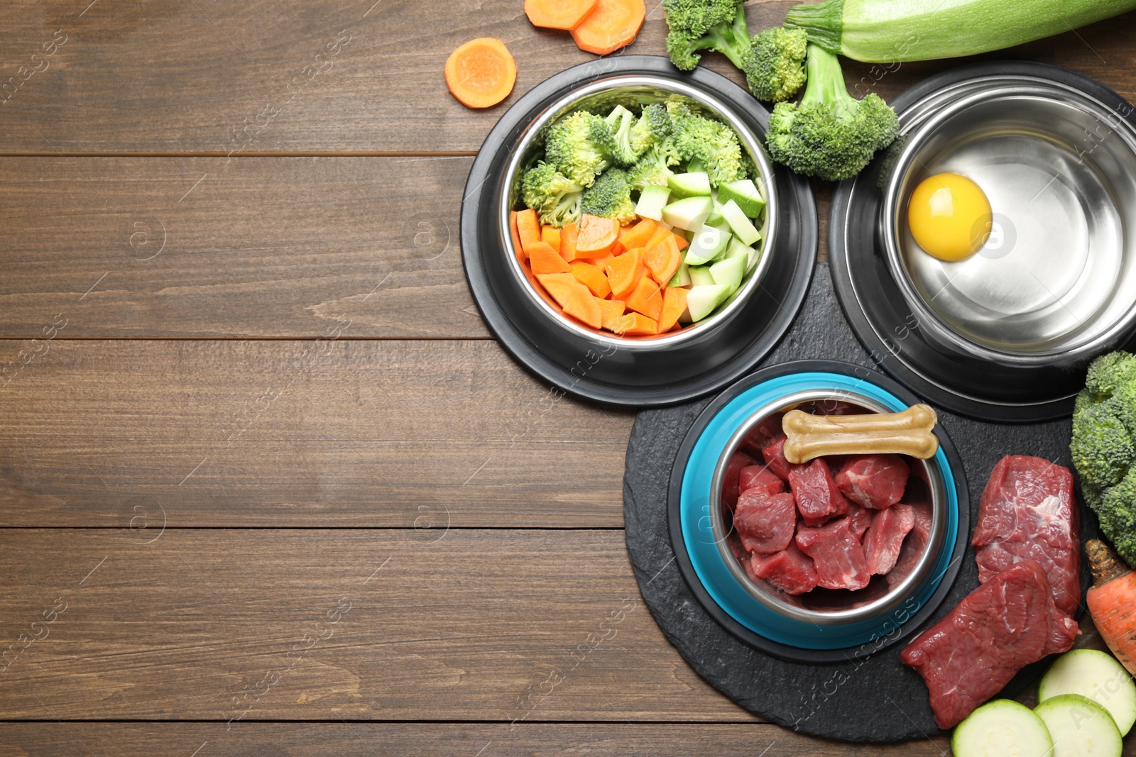 Photo of Natural pet food in feeding bowls and products on wooden table, flat lay. Space for text