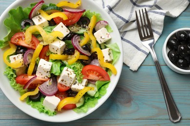 Photo of Delicious fresh Greek salad served on light blue wooden table, flat lay