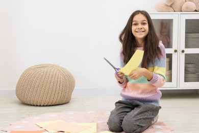 Photo of Girl cutting figure out of color paper for her creative project at home. Art and craft