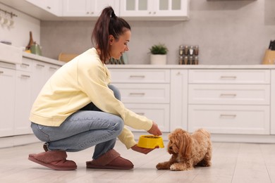 Photo of Smiling owner feeding her cute dog with dry pet food in kitchen