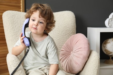 Photo of Cute little boy with telephone handset in armchair indoors