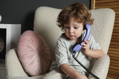 Photo of Cute little boy with telephone handset in armchair indoors