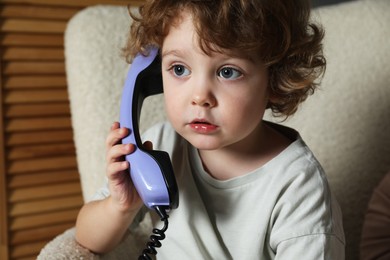 Photo of Cute little boy with telephone handset in armchair indoors