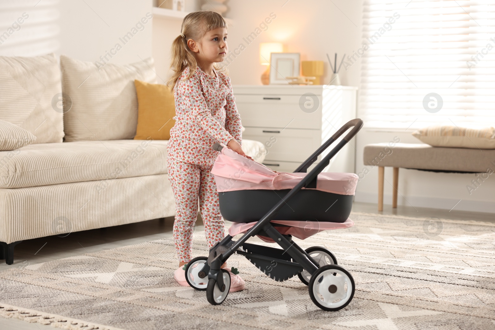 Photo of Cute little girl with doll stroller at home