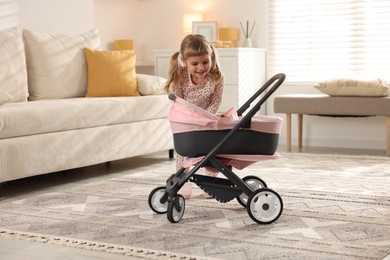 Photo of Cute little girl with doll stroller at home