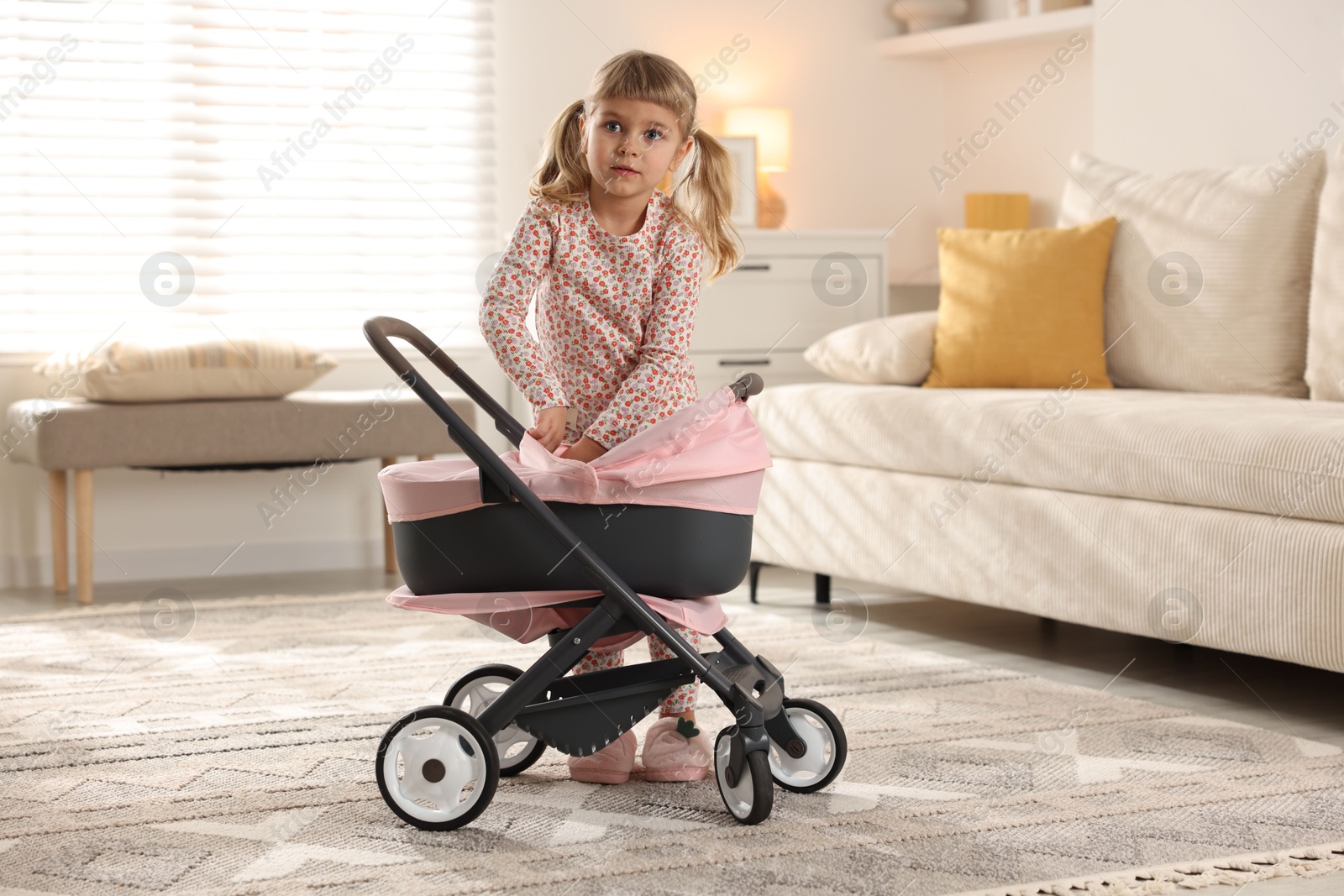 Photo of Cute little girl with doll stroller at home