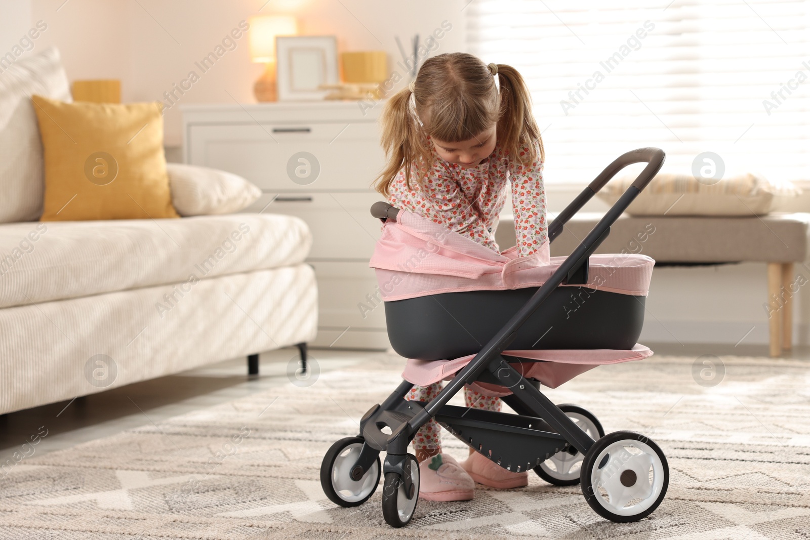 Photo of Cute little girl with doll stroller at home