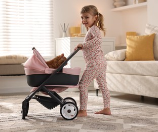 Photo of Cute little girl with her ginger cat in doll stroller at home