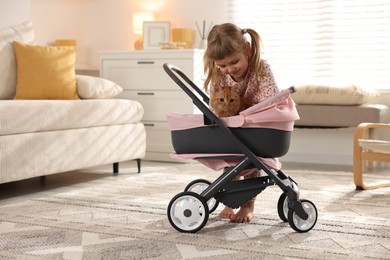 Photo of Cute little girl with her ginger cat in doll stroller at home