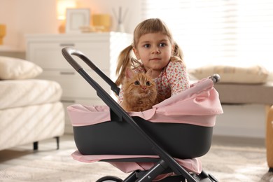 Photo of Cute little girl with her ginger cat in doll stroller at home