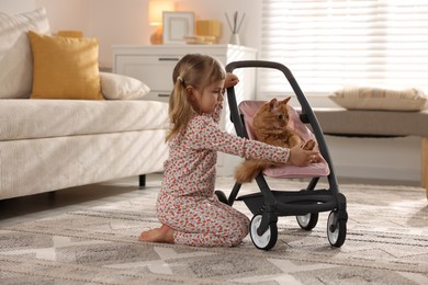 Photo of Cute little girl with her ginger cat in doll stroller at home