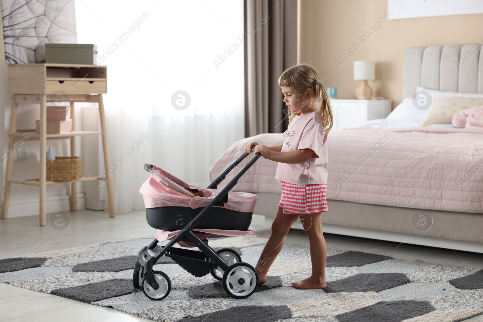 Photo of Cute little girl with doll stroller at home