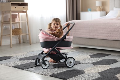 Photo of Cute little girl with her ginger cat in doll stroller at home