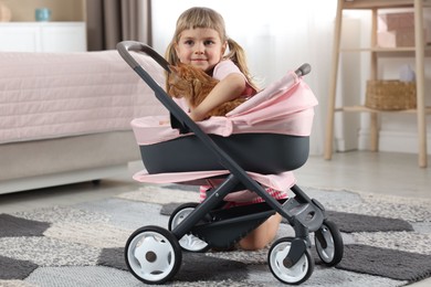 Photo of Cute little girl with her ginger cat in doll stroller at home