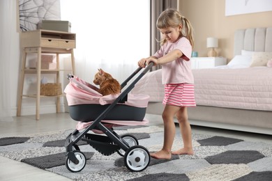 Photo of Cute little girl with her ginger cat in doll stroller at home