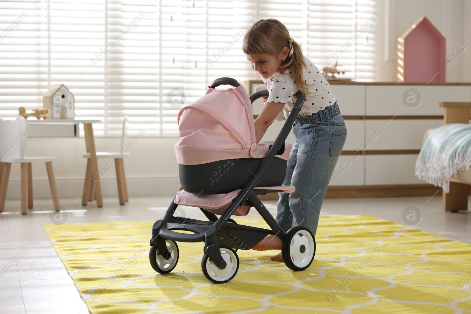 Photo of Cute little girl with doll stroller at home