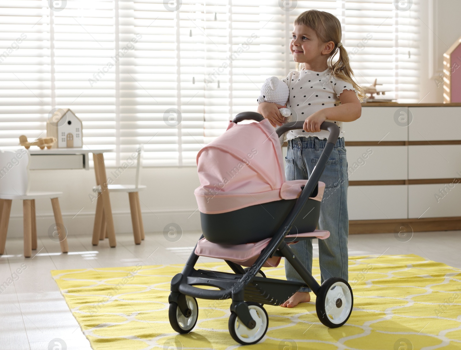 Photo of Cute little girl with doll stroller and teddy bear at home