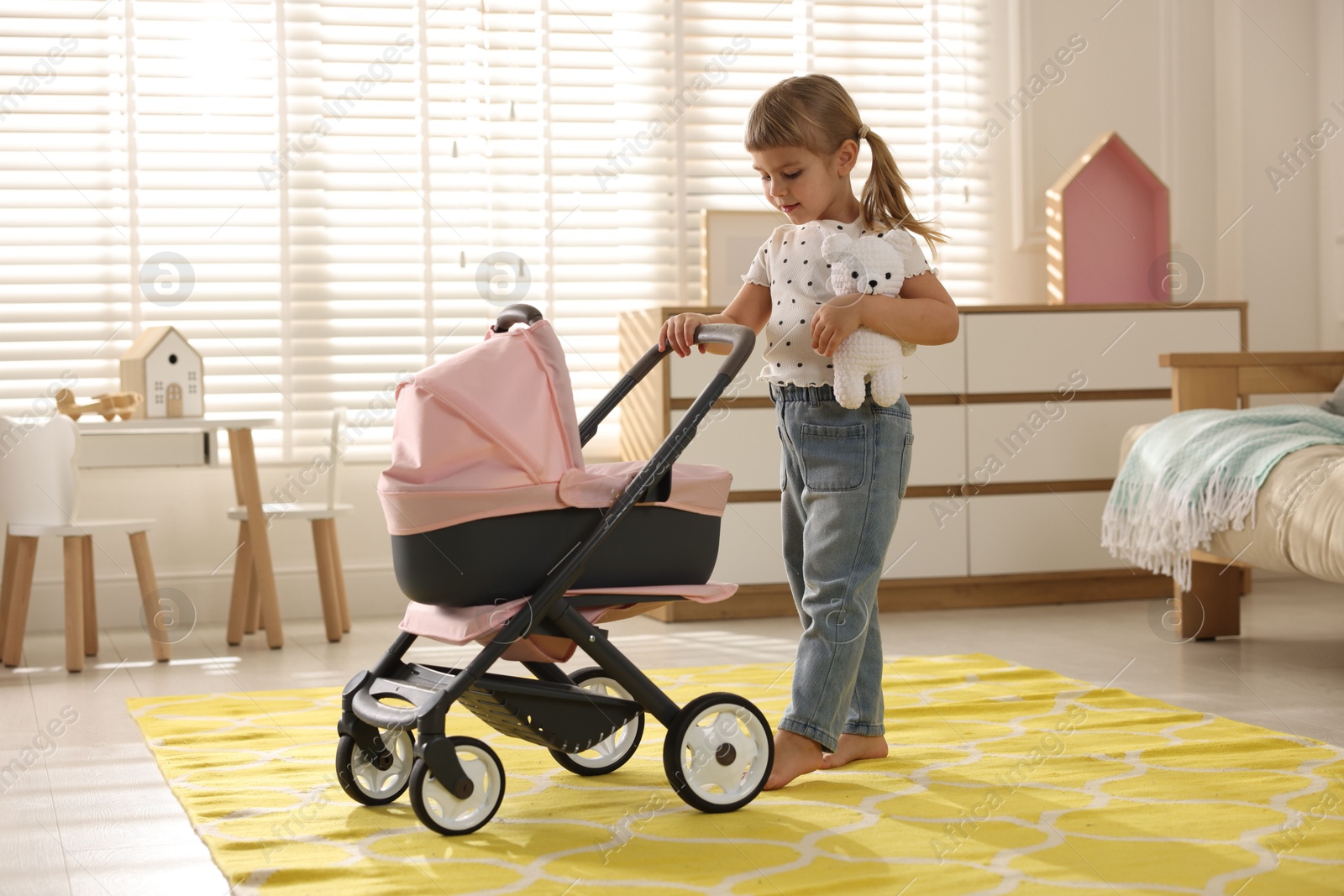 Photo of Cute little girl with doll stroller and teddy bear at home