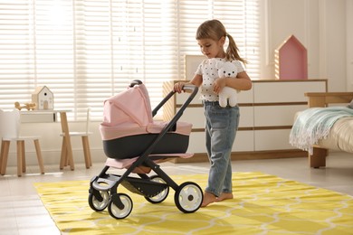 Photo of Cute little girl with doll stroller and teddy bear at home