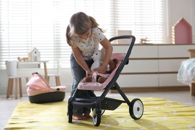 Photo of Cute little girl playing with doll stroller and teddy bears at home