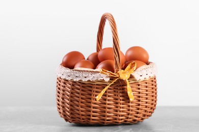 Photo of Wicker basket with fresh eggs on grey marble table against white background, closeup