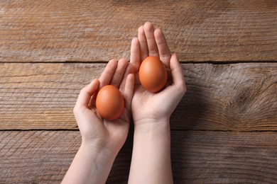 Photo of Woman with raw eggs at wooden table, top view