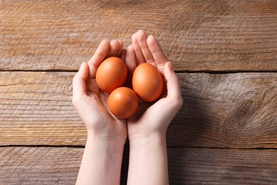 Photo of Woman with raw eggs at wooden table, top view