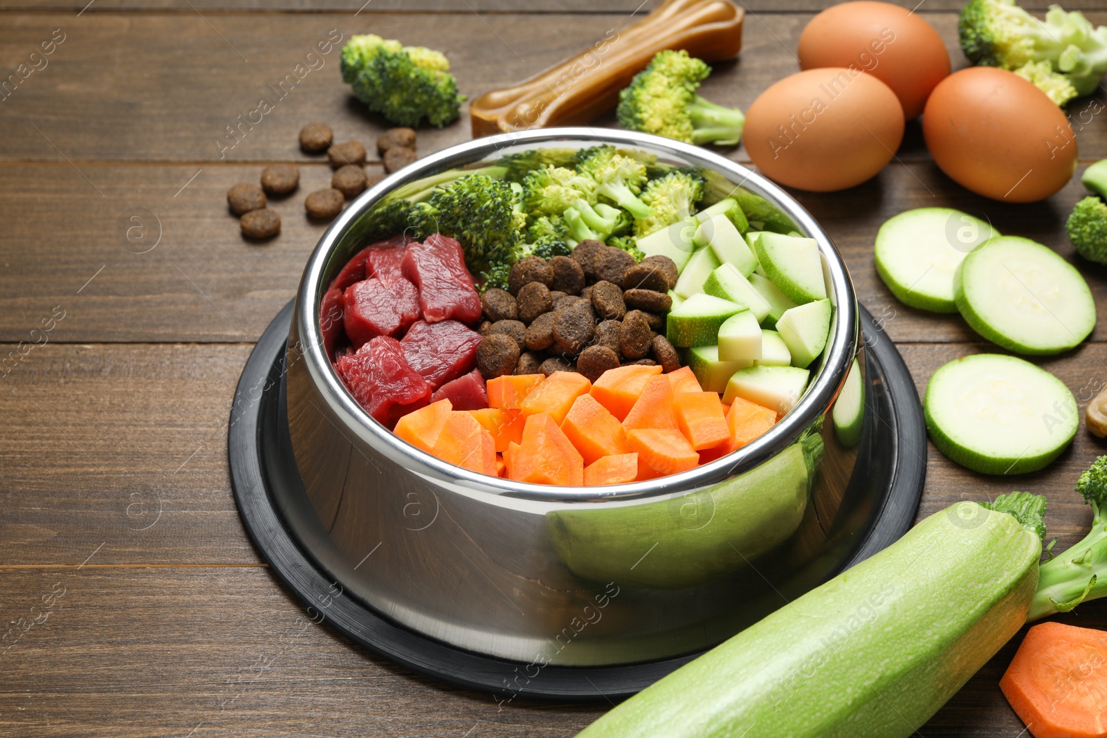 Photo of Dry and natural pet food in feeding bowl among products on wooden table, closeup