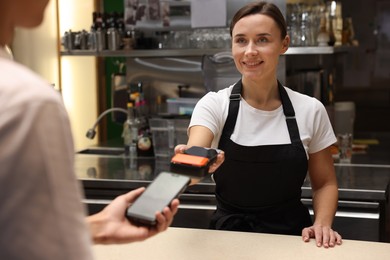 Photo of Cafe worker taking payment from client via terminal indoors