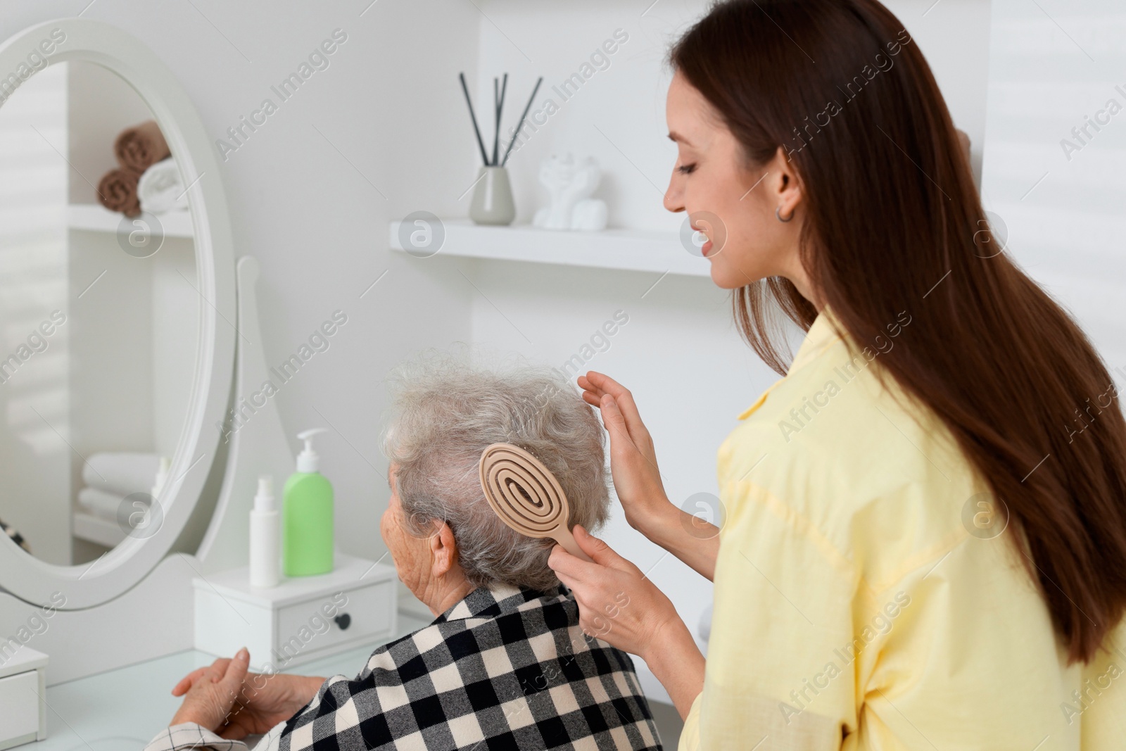 Photo of Woman brushing senior lady with brush indoors