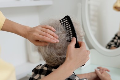 Photo of Woman brushing senior lady with comb indoors, closeup