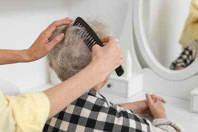 Photo of Woman brushing senior lady with comb indoors, closeup