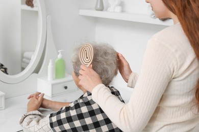 Photo of Granddaughter brushing her grandmother with brush at home, closeup