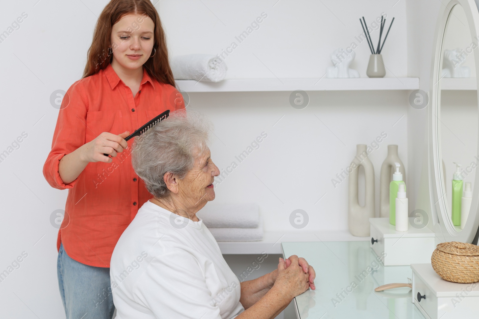 Photo of Granddaughter brushing her grandmother with comb at home