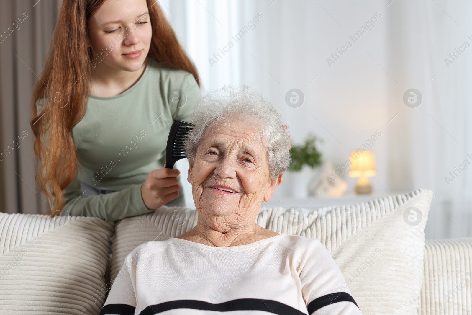 Photo of Granddaughter brushing her grandmother with comb at home. Space for text