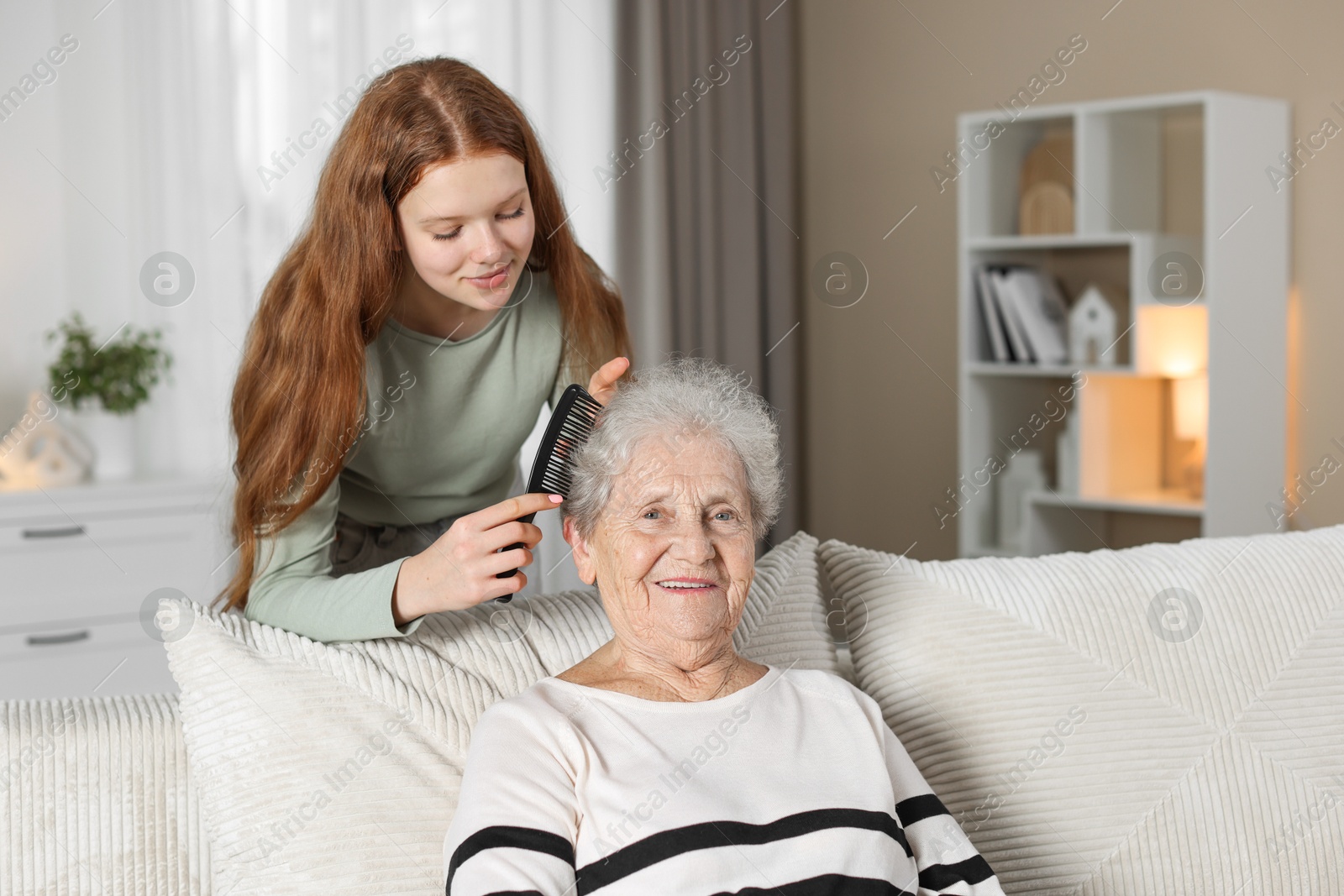 Photo of Granddaughter brushing her grandmother with comb at home