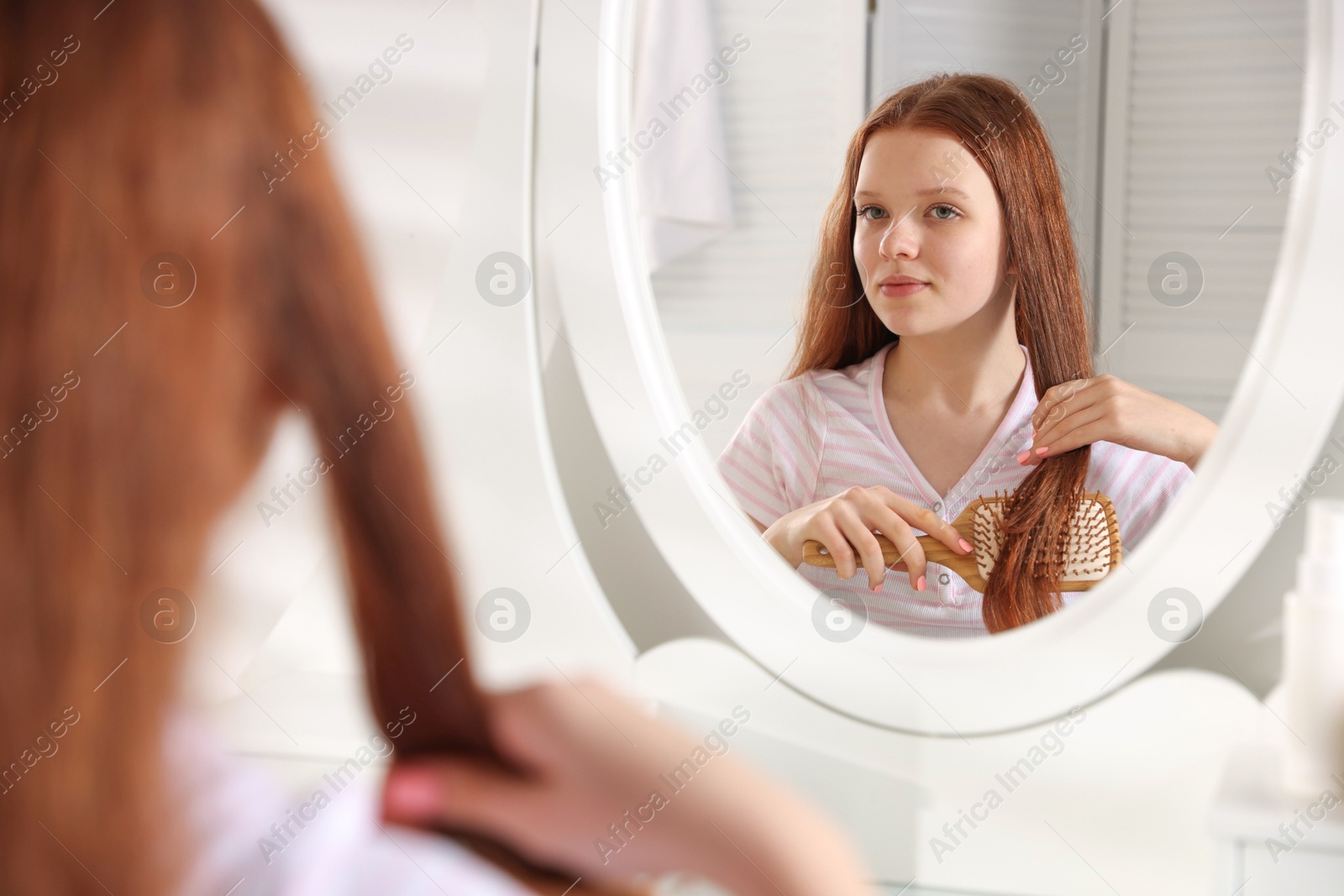 Photo of Beautiful teenage girl brushing her hair near mirror at home, selective focus