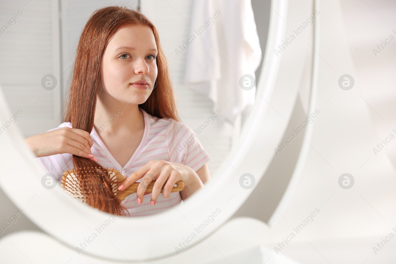 Photo of Beautiful teenage girl brushing her hair near mirror at home