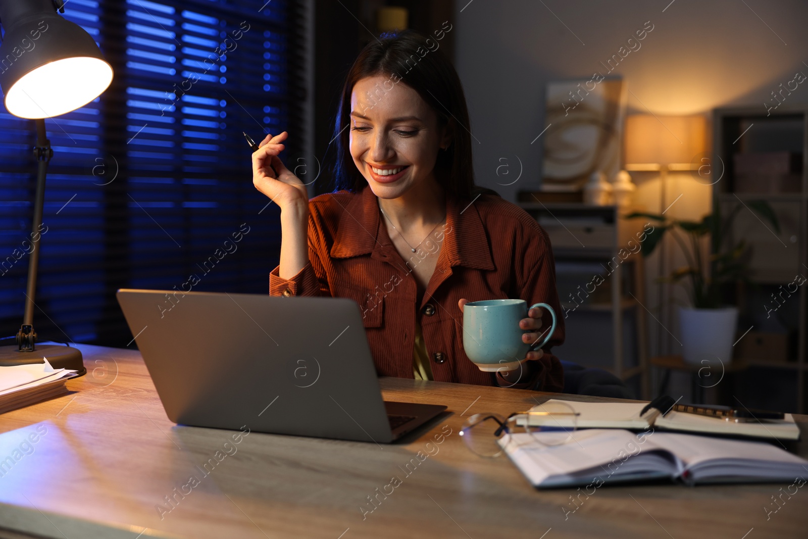 Photo of Woman with cup of coffee working on laptop at desk in home office