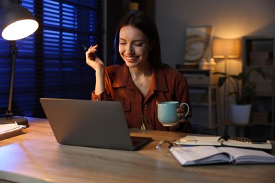 Photo of Woman with cup of coffee working on laptop at desk in home office