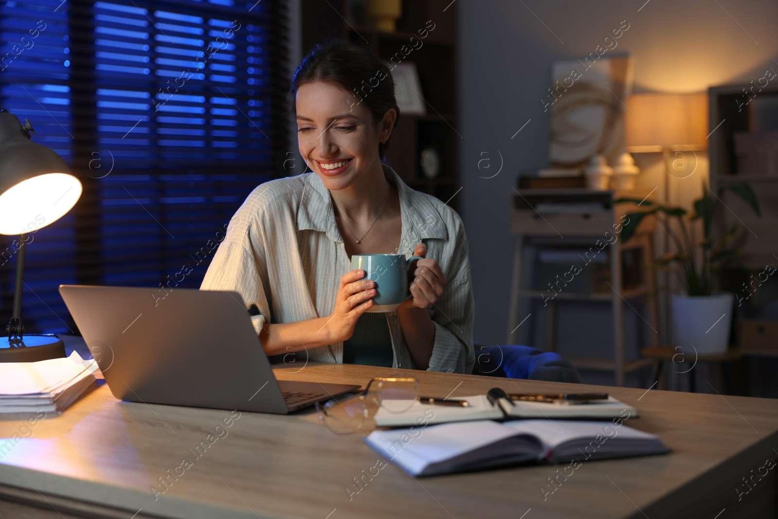 Photo of Woman with cup of coffee working on laptop at desk in home office